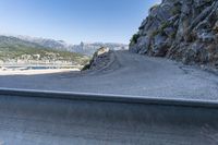 a car drives along a road that is close to a mountain and a large bay