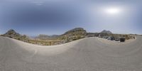 a panorama picture of an empty road surrounded by mountains with traffic and trees on both sides