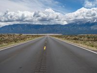 an open empty highway in the middle of the mountains with blue skies and fluffy white clouds