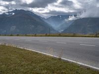 the car is driving down the highway by the mountains on a cloudy day with fog over the peaks