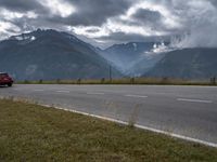 the car is driving down the highway by the mountains on a cloudy day with fog over the peaks