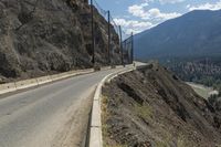 a couple of people walking across a bridge next to a mountain side road with cars going by