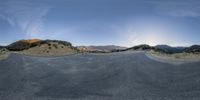 a curved road through the desert with mountains in the background and clouds above it and a car parked on the street