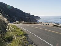 an empty highway with yellow stripes passes the ocean along a coastal trail by a steep hillside