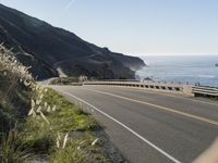 an empty highway with yellow stripes passes the ocean along a coastal trail by a steep hillside