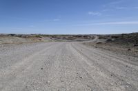 a dirt road is surrounded by some hills and desert like terrain as the vehicle sits on it