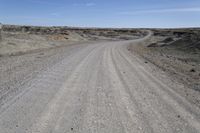 a dirt road is surrounded by some hills and desert like terrain as the vehicle sits on it