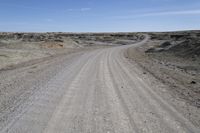 a dirt road is surrounded by some hills and desert like terrain as the vehicle sits on it