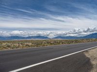 a man standing on the side of the road next to an empty highway with a mountain range behind him