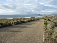 a paved road near the ocean on a partly cloudy day with no traffic to pass