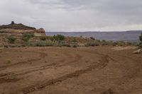 a small dirt path going through the desert with mountains in the background on a grey cloudy day