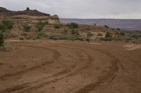 a small dirt path going through the desert with mountains in the background on a grey cloudy day