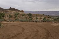 a small dirt path going through the desert with mountains in the background on a grey cloudy day