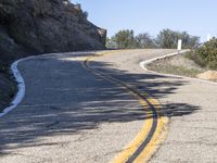 a yellow curve and some rock side next to the highway with a black sign on it