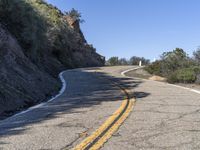 a yellow curve and some rock side next to the highway with a black sign on it