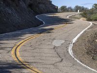 a yellow curve and some rock side next to the highway with a black sign on it