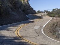 a yellow curve and some rock side next to the highway with a black sign on it