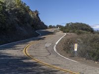 a yellow curve and some rock side next to the highway with a black sign on it