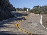 a yellow curve and some rock side next to the highway with a black sign on it