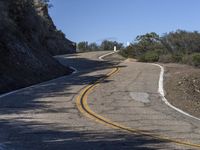 a yellow curve and some rock side next to the highway with a black sign on it