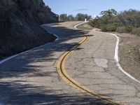 a yellow curve and some rock side next to the highway with a black sign on it