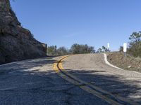 a yellow curve and some rock side next to the highway with a black sign on it