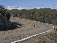 a yellow curve and some rock side next to the highway with a black sign on it