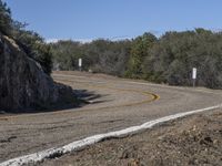 a yellow curve and some rock side next to the highway with a black sign on it