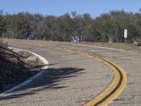 a yellow curve and some rock side next to the highway with a black sign on it