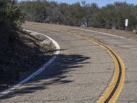 a yellow curve and some rock side next to the highway with a black sign on it