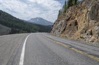 a long winding road with white lines through the mountains and pine covered cliffs behind it