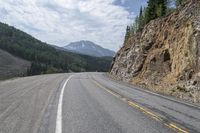 a long winding road with white lines through the mountains and pine covered cliffs behind it