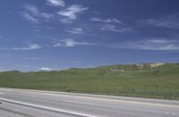 a sign on a rural highway that has grass and hills in the background of the scene
