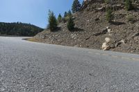 an asphalt highway on a mountain with rocks and grass next to it and trees growing on the side