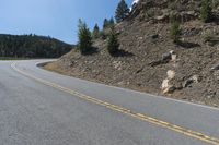 an asphalt highway on a mountain with rocks and grass next to it and trees growing on the side