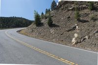 an asphalt highway on a mountain with rocks and grass next to it and trees growing on the side