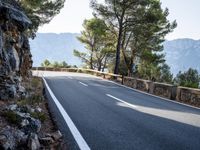 a very long empty highway on the side of the mountain slope by itself in front of a cliff wall