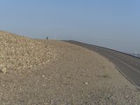 a highway with rocks and gravel on the side, which is beside the road, there is no traffic and water in the distance