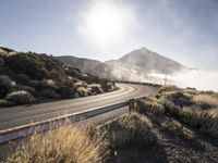 a bendy highway with cars driving along the side of it and mist swirling over the mountains