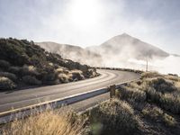 a bendy highway with cars driving along the side of it and mist swirling over the mountains