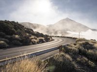 a bendy highway with cars driving along the side of it and mist swirling over the mountains