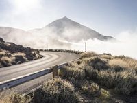 a bendy highway with cars driving along the side of it and mist swirling over the mountains