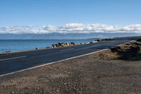 a scenic highway near the water that is very wide by the shoreline and to the mountains