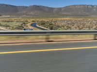 a motorcycle rider rides a motorcycle down the highway, surrounded by mountains and hills during daytime