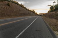 a highway stretches off a hill to the horizon at sunset, with a lone cyclist and some hills in the distance