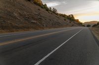 a highway stretches off a hill to the horizon at sunset, with a lone cyclist and some hills in the distance