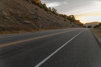 a highway stretches off a hill to the horizon at sunset, with a lone cyclist and some hills in the distance