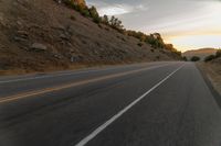 a highway stretches off a hill to the horizon at sunset, with a lone cyclist and some hills in the distance