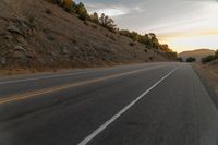 a highway stretches off a hill to the horizon at sunset, with a lone cyclist and some hills in the distance