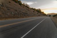 a highway stretches off a hill to the horizon at sunset, with a lone cyclist and some hills in the distance